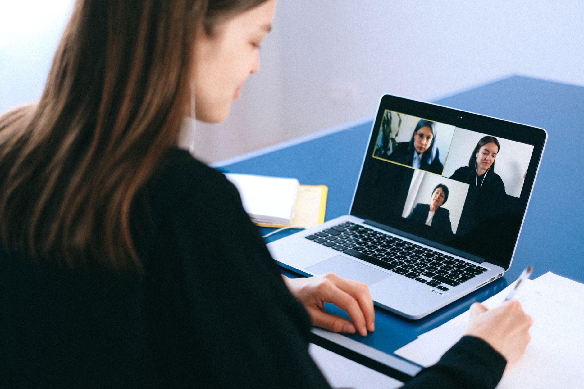 A woman on a video call at her laptop taking notes