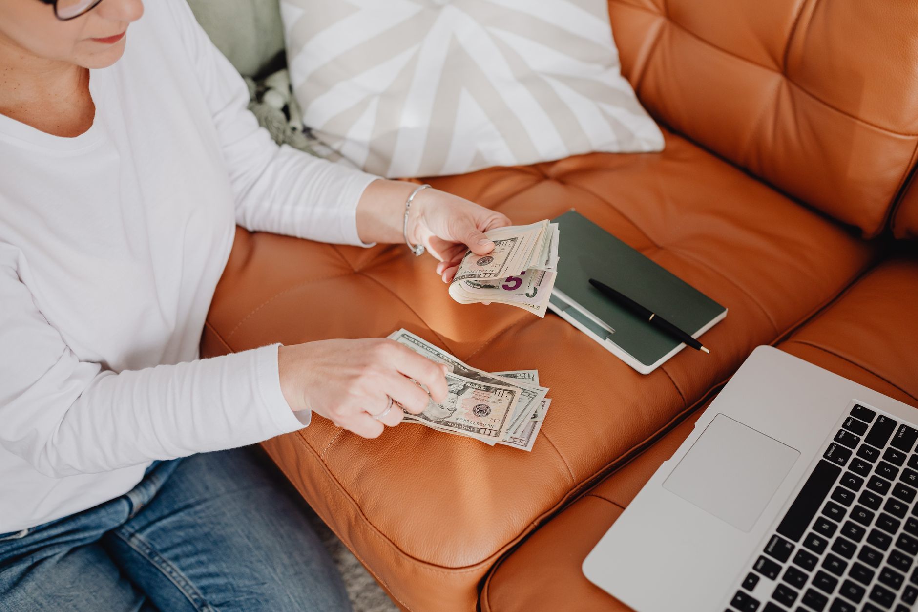 A person counting cash beside an open laptop