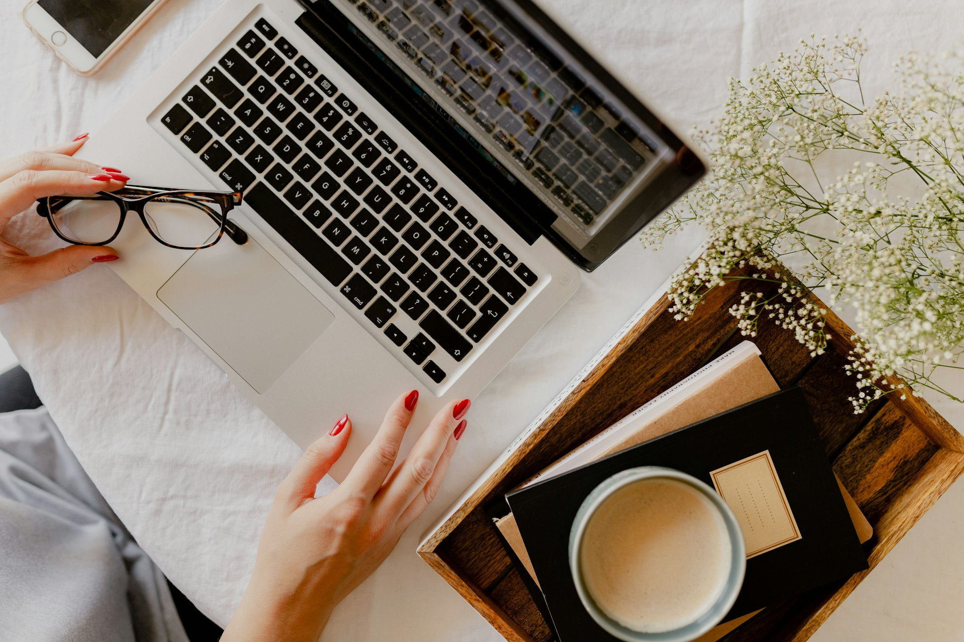 A woman's hand on a laptop beside a coffee and flowers