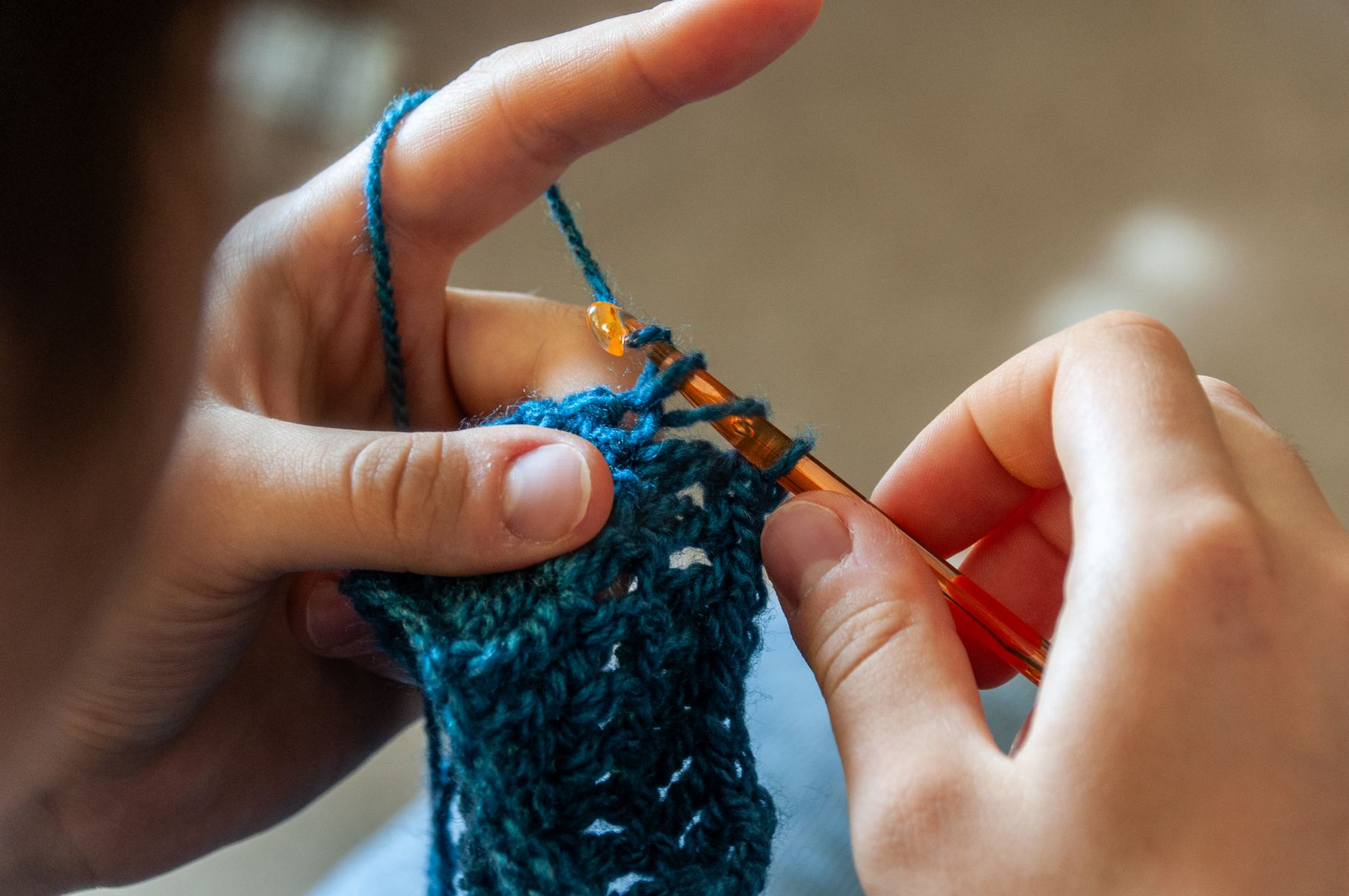 Hands crocheting a blue yarn piece with a crochet hook