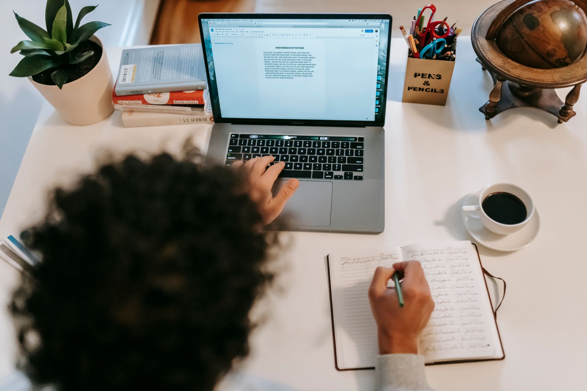 A writer typing on a laptop beside a notebook and coffee