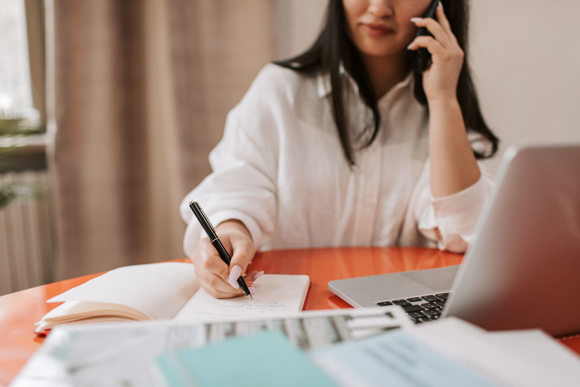 A woman taking notes on a call beside her laptop