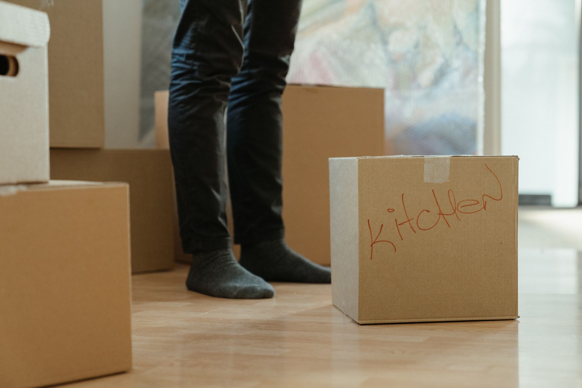 A person standing among moving boxes labeled for the kitchen