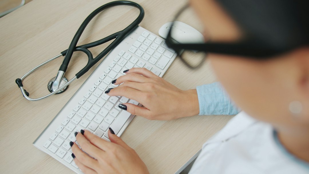 A doctor typing on a keyboard with a stethoscope nearby