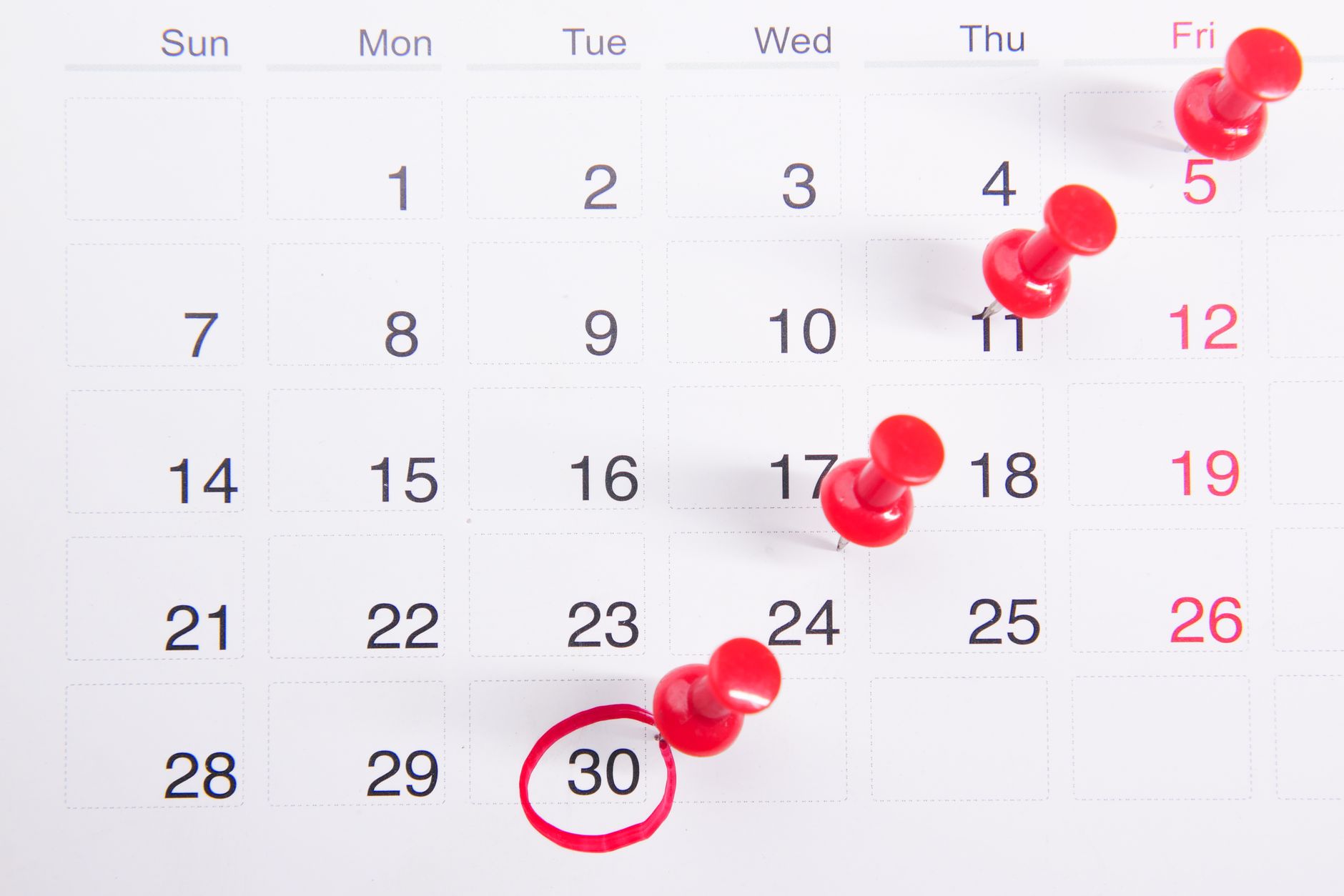 A calendar with red push pins marking dates